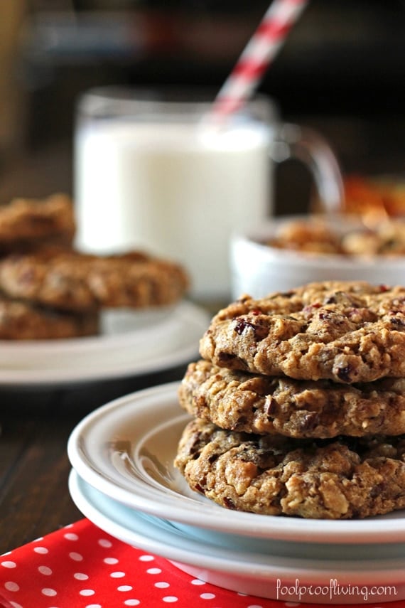 A few chunky oatmeal cookies are placed on top of each other with a glass of milk