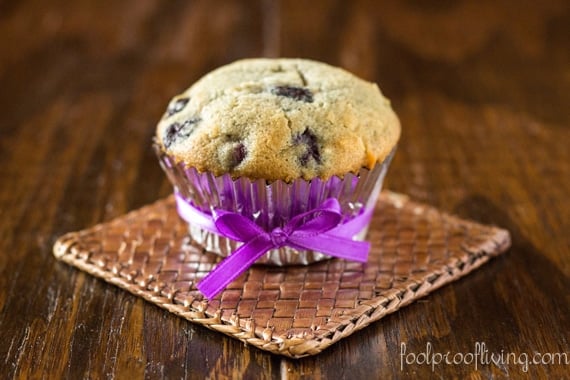 A coconut and blueberry muffin finished resting on a coaster on a table.