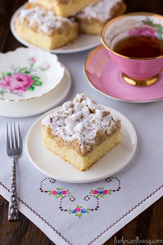 A slice of New York-Style Crumb Cake placed on a plate and served with tea on the side.