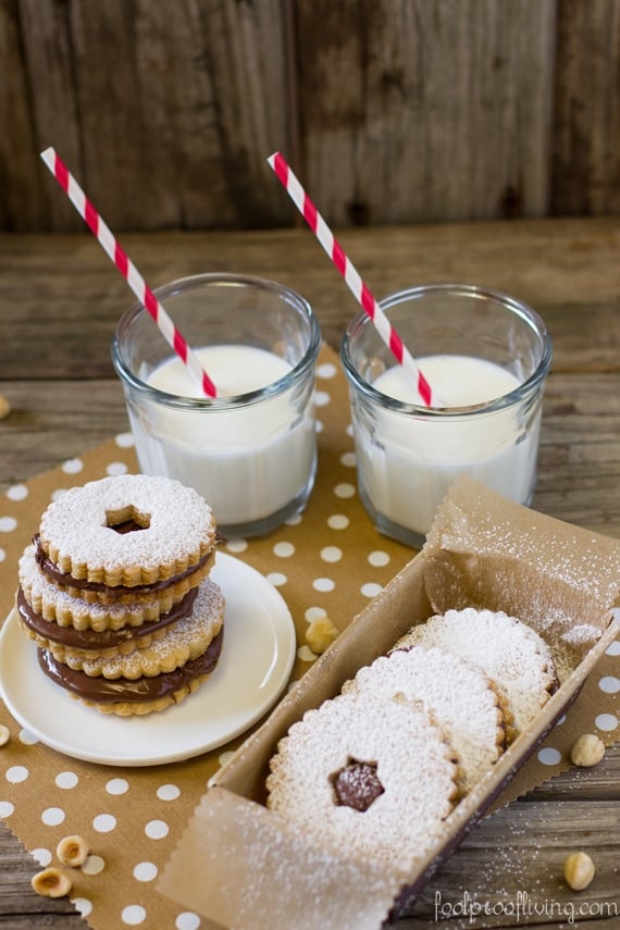 Three Nutella Sandwich Cookies on a plate and three sandwich cookies in a box with 2 glasses of milk in the background