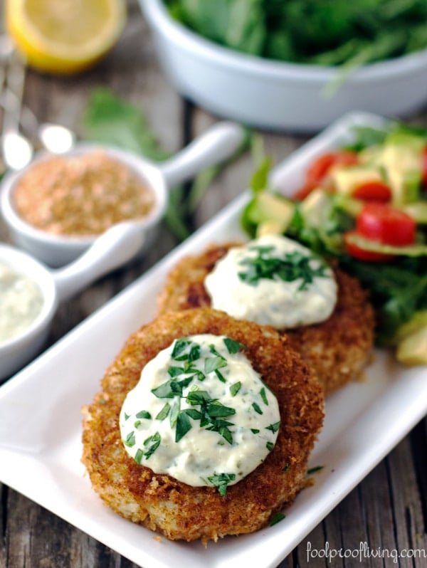 Two Crab Cakes with Rémoulade Sauce with avocado and tomato salad and condiments on the side