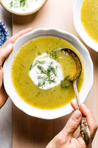 Cream of zucchini soup in a bowl photographed as a person is spooning in it.