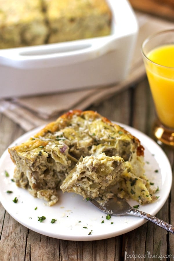 Close up shot of Eggs with Artichoke, Tarragon, and Parmesan serving on a plate with a fork and orange juice and dish in a platter in the background