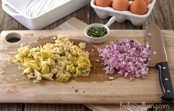 Sliced Artichoke Hearts, Chopped Tarragon, and Chopped Onions with a knife on a cutting board and eggs in the background  