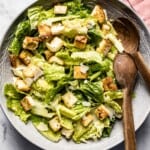 Traditional Caesar Salad in a bowl with wooden spoons on the side