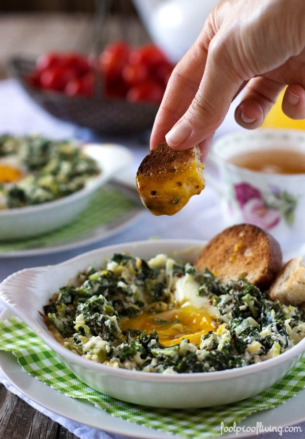 Baked Eggs with Kale and Leeks with a piece of bread being dunked and bread on the side 