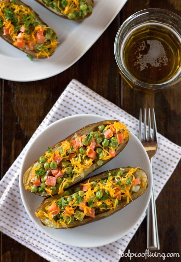 2 Loaded Twice-Baked Potato Skins on a plate 2 more baked potato skins on another plate with a fork on a napkin and a glass of beer on the side