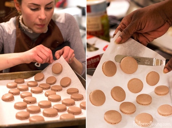 A woman is removing macarons from parchment paper