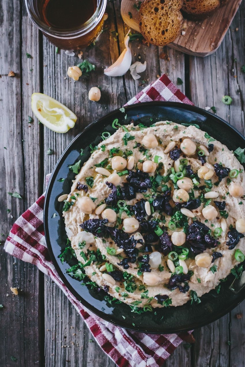 A plate of Homemade Mediterranean Hummus garnished with olives, pine nuts and scallion