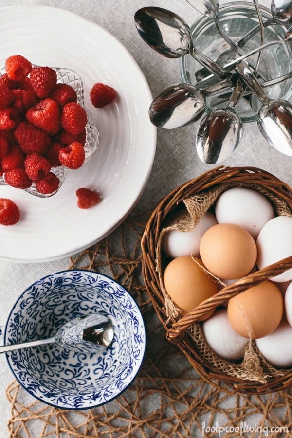 Eggs in a basket and raspberries in a bowl with a small empty bowl for waffles