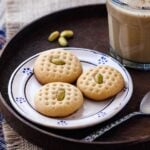 Three Tahini Cookies with Pistachios with a glass of chocolate milk and pistachios on the side