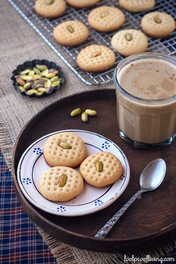 Tahini Cookies with Pistachios on a plate with more on a cooling rack with pistachios and a glass of chocolate milk on the side