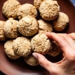 Almond flour tahini cookies on a plate with a person taking one cookie from the plate.