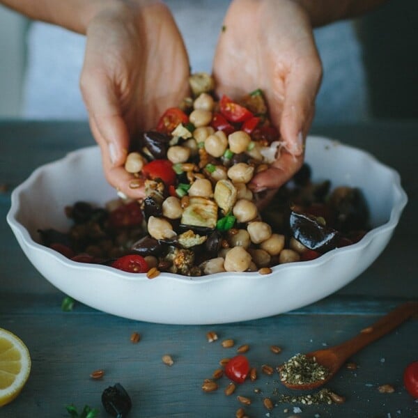 Person pouring ingredients by hand into Mediterranean Chickpea, Farro, and Za'atar Salad