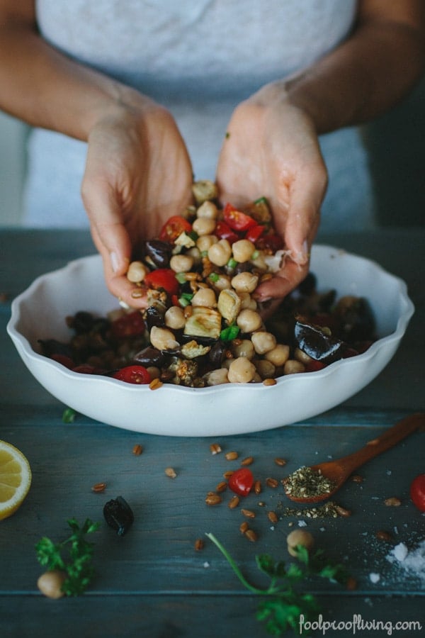 Person pouring ingredients by hand into Mediterranean Chickpea, Farro, and Za'atar Salad