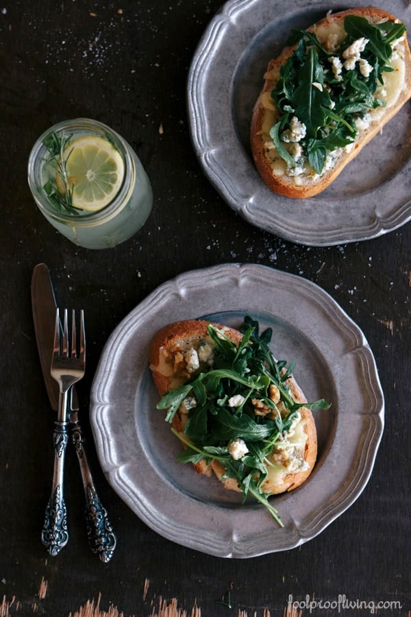 Two slices of Gorgonzola-Walnut Bruschetta with Truffle Oil on two plates with flatware on the side