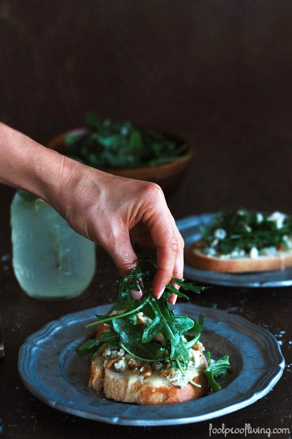 Person placing greens on top of Gorgonzola-Walnut Bruschetta with Truffle Oil