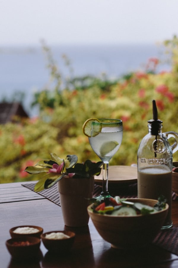 One scene of small garden salad in a bowl with a beverage and salad dressing the background. Another scene of a person holding a tray with 2 salads and a bottle of dressing 