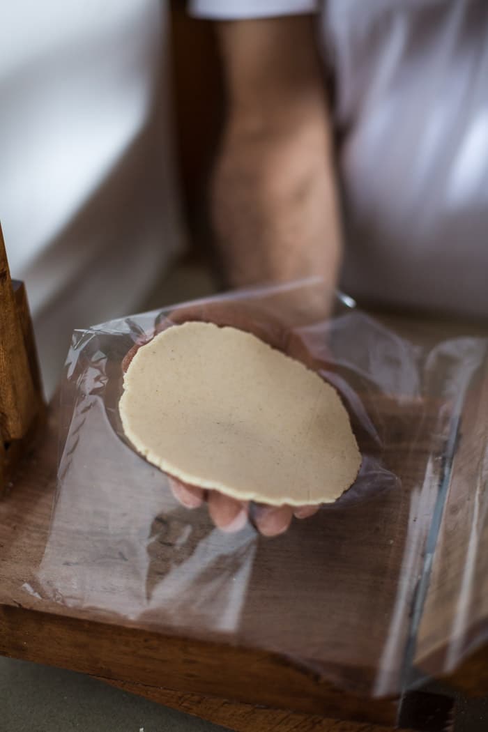 A man is showing flattened corn tortilla to show the steps to Making corn tortillas at home