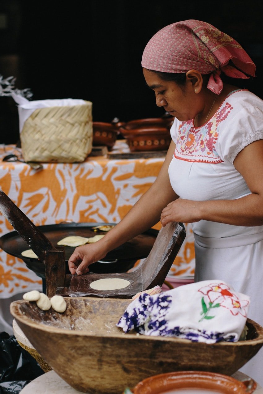 Woman makes corn tortillas by hand and cooks them on a large clay