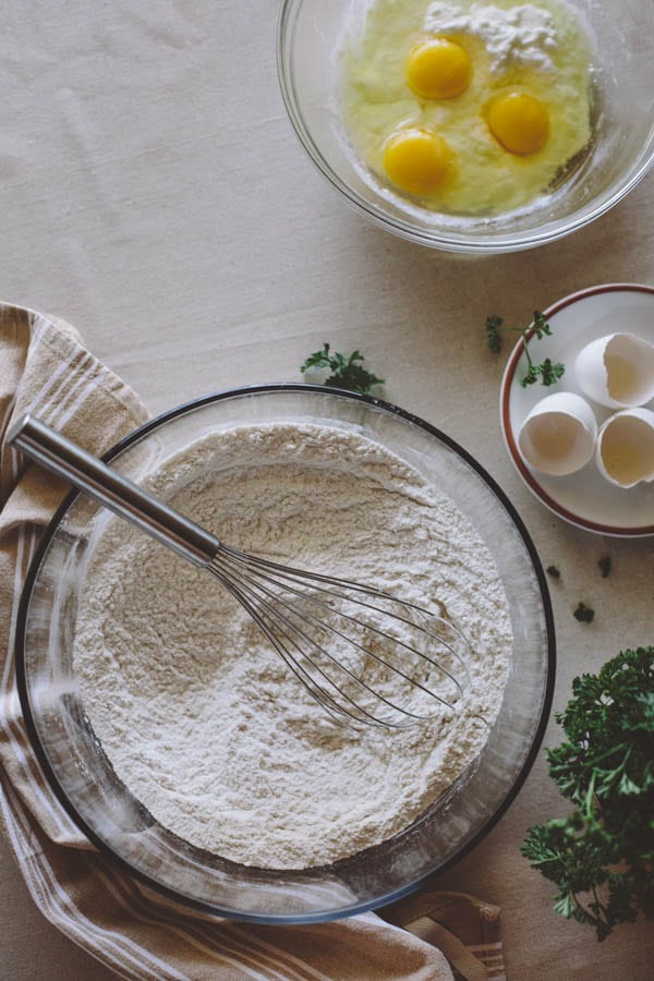 Bowl of flour with a whisk and cracked eggs on the side