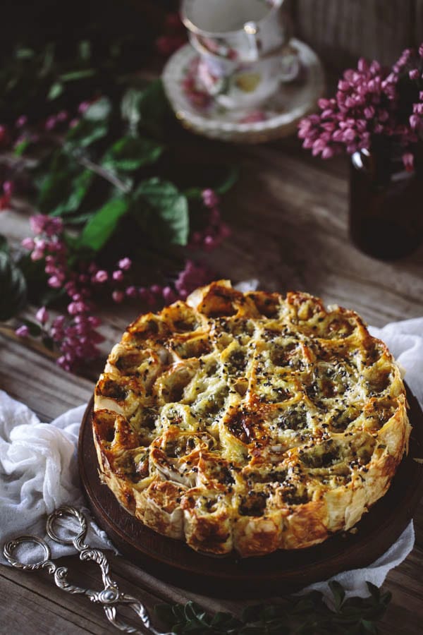 Cheesy Parsley Phyllo Rolls on a plate on a table with tongs, cloth napkin and decorative flowers