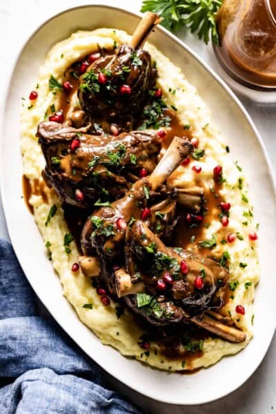 Lamb shanks on a serving plate with mashed potatoes from the top view.