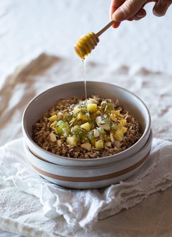 A bowl of Almond-Kasha Porridge with Ginger and Pineapple with honey being drizzled