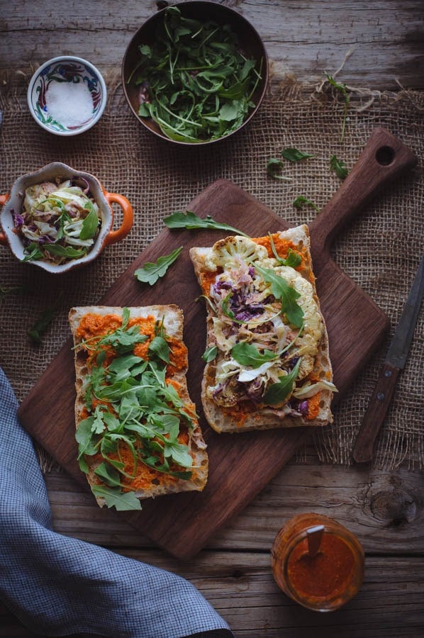 Two Cauliflower Steak Sandwich with Romesco Sauce on a cutting board with a small 