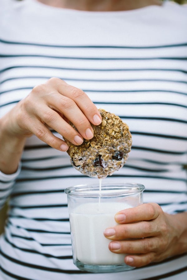 a woman is dipping a vegan breakfast bar into milk