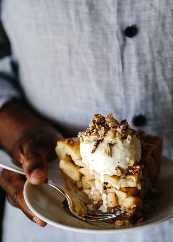 Person holding a slice Caramel Apple Pie with a scoop of ice cream on a small plate