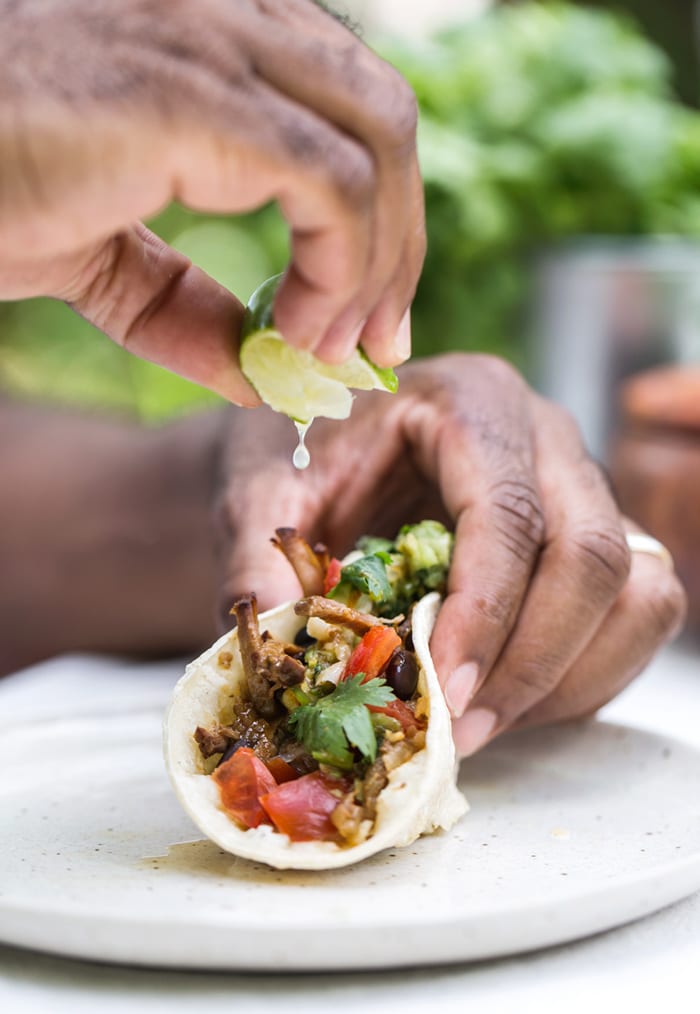 A man is squeezing lime in to Slow Cooker Beef Brisket Tacos 