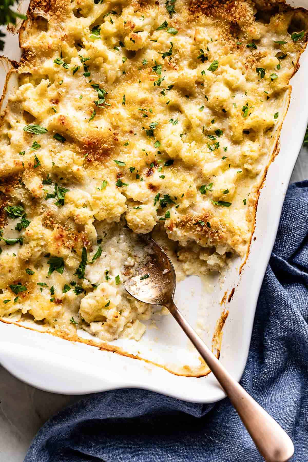 Cauliflower au gratin in a casserole dish with a spoon on the side.