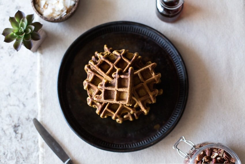 A plate of Spicy Pumpkin Waffles with syrup, nuts, small flowers and a knife on the side 