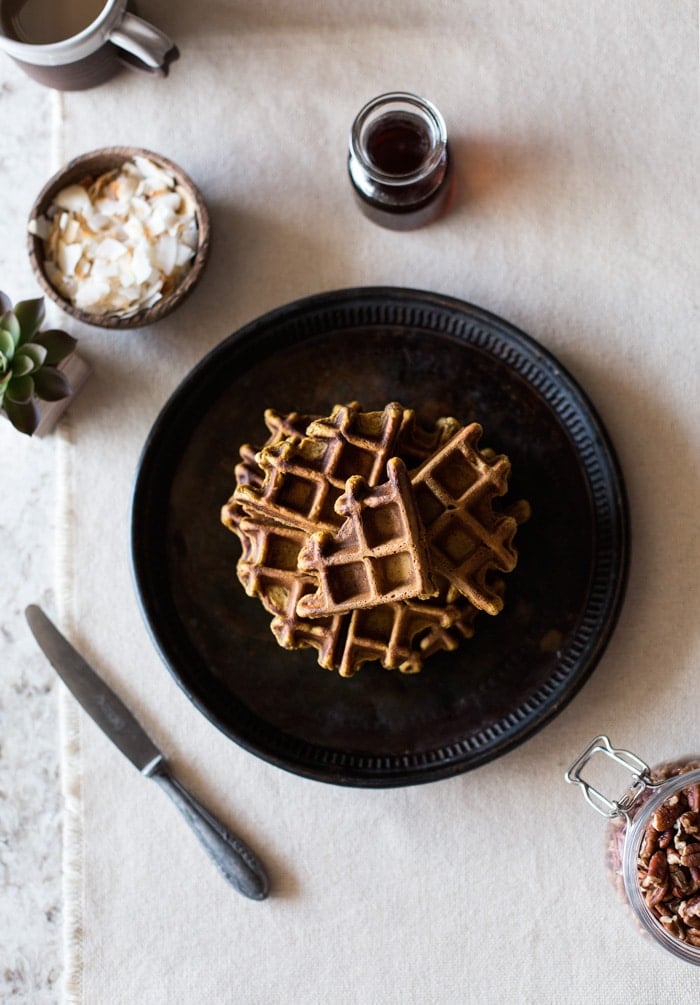 A plate Pumpkin Waffles with Coconut Whipped Cream and a small jar of syrup with coconut shavings