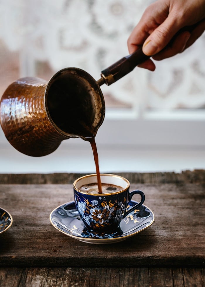 A woman is pouring freshly cooked Turkish coffee from cezve