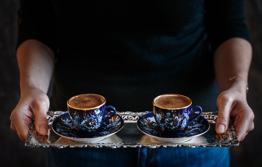 A woman is serving two cups of coffee on a tray