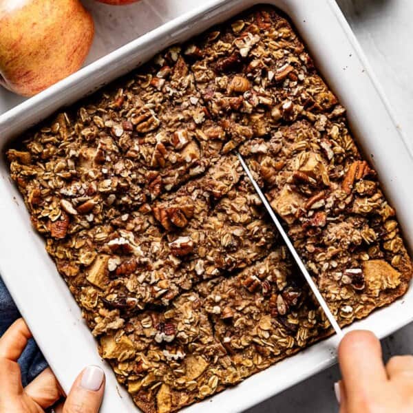Apple cinnamon baked oatmeal being sliced by a person from the top view.