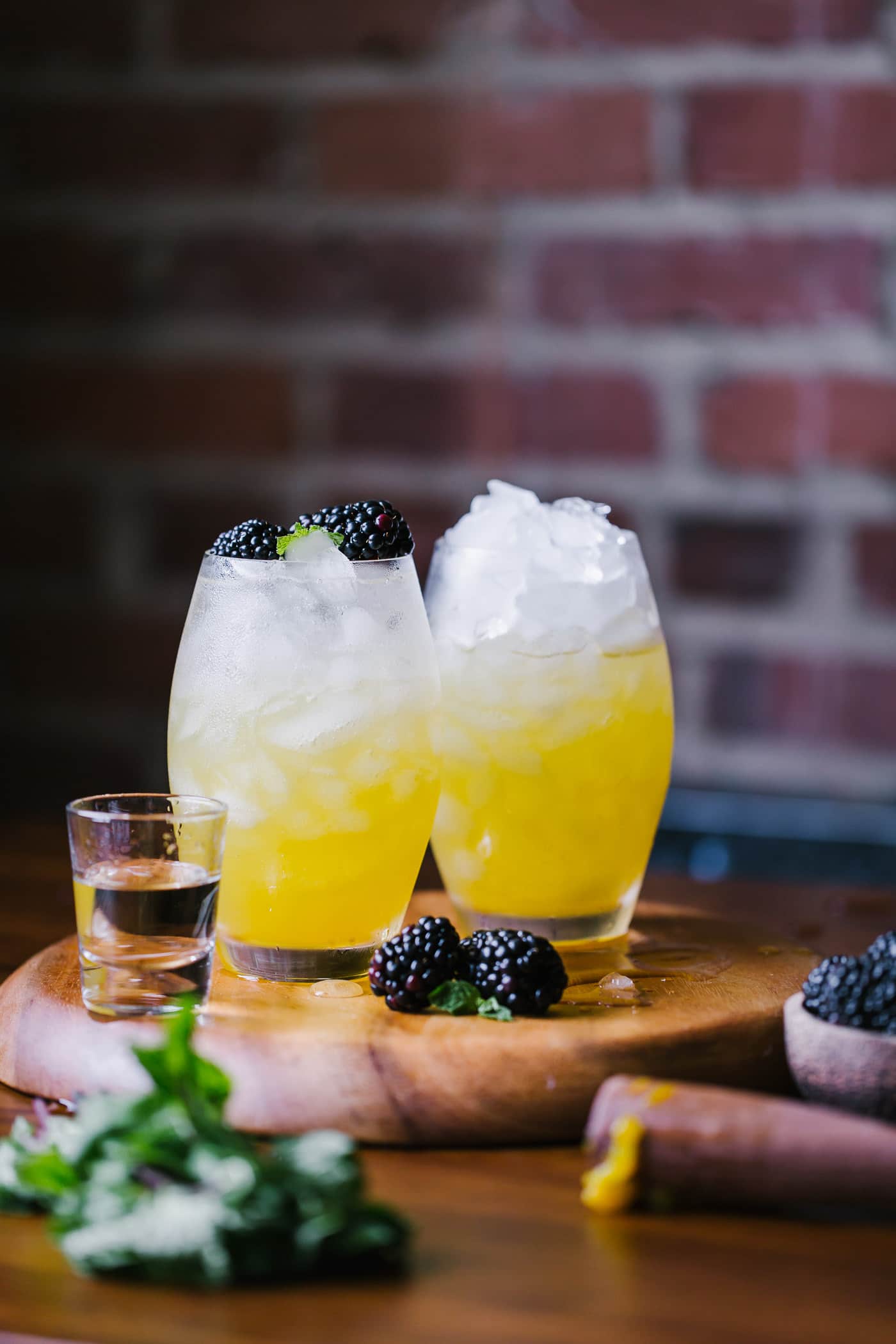 Two glass of mango and blackberry vodka cooler garnished with fresh blackberries photographed side by side  from the front view.