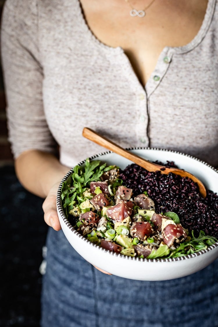 a woman is serving a bowl black Rice Recipe topped off with tuna