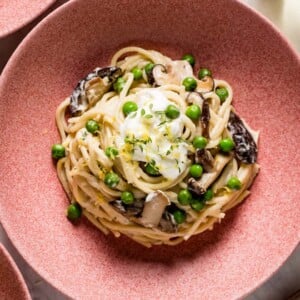 A bowl of creamy pasta with peas and mushrooms topped off with ricotta cheese