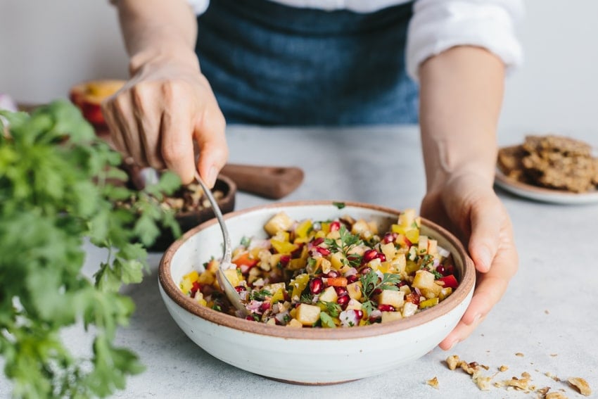 Person stirring a bowl of Fresh Peach and Walnut Salsa