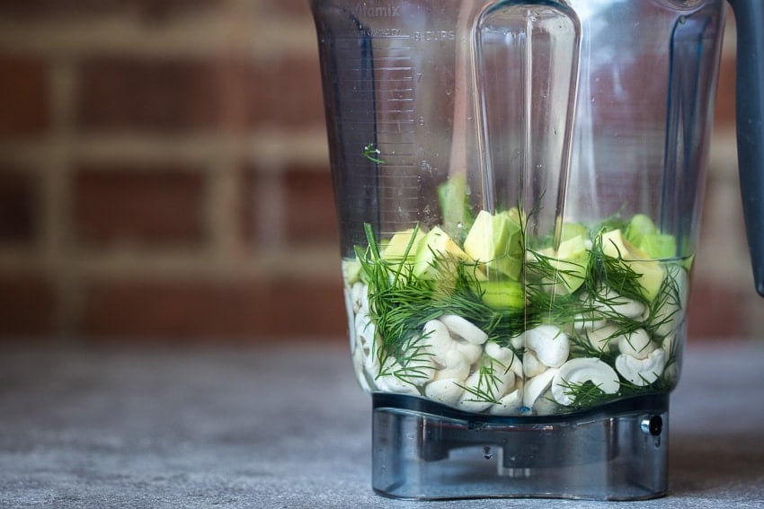 Side view of cashew, avocado, herbs in a Vitamix