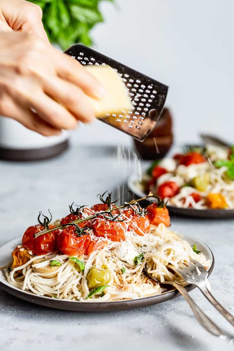 A woman is grating parmesan on a plate of Caprese Pasta Salad