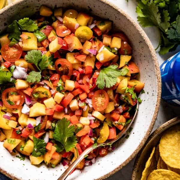 fresh peach salsa placed in a bowl with chips and beer on the side