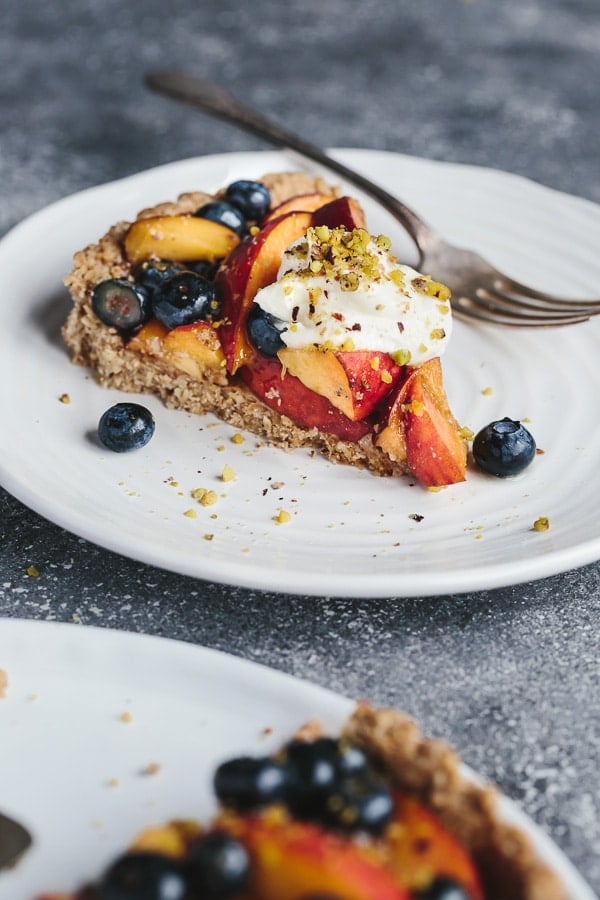 A slice of Fresh Peach and Blueberry Tart with Walnut Crust on a plate with a fork