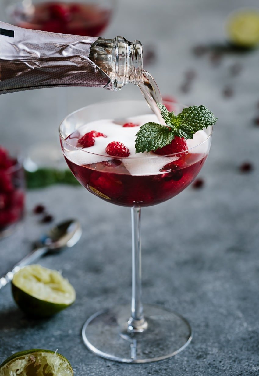 A woman is pouring champagne to top off Raspberry and Pomegranate Rosé Summer Cocktail