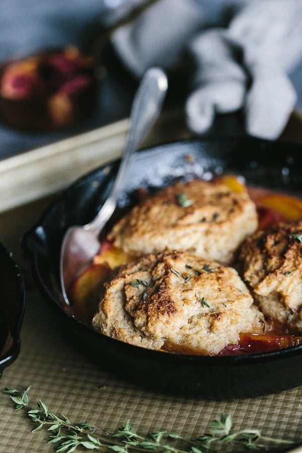 Peach Cobbler with Cornmeal Thyme Biscuits placed in a cast iron skillet with a spoon