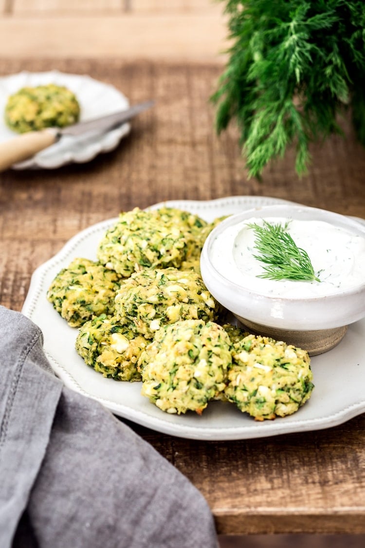 A plate with Baked courgette Fritters with Feta and Dill are served with yogurt sauce and photographed from the front.