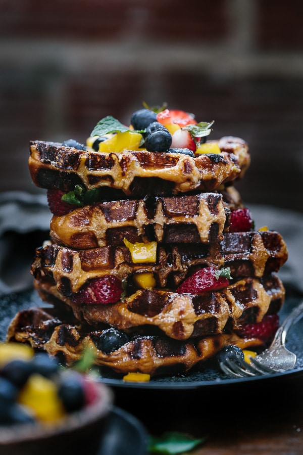 A batch of brioche waffles recipe made and slices of it is layered with fruit and herbs.